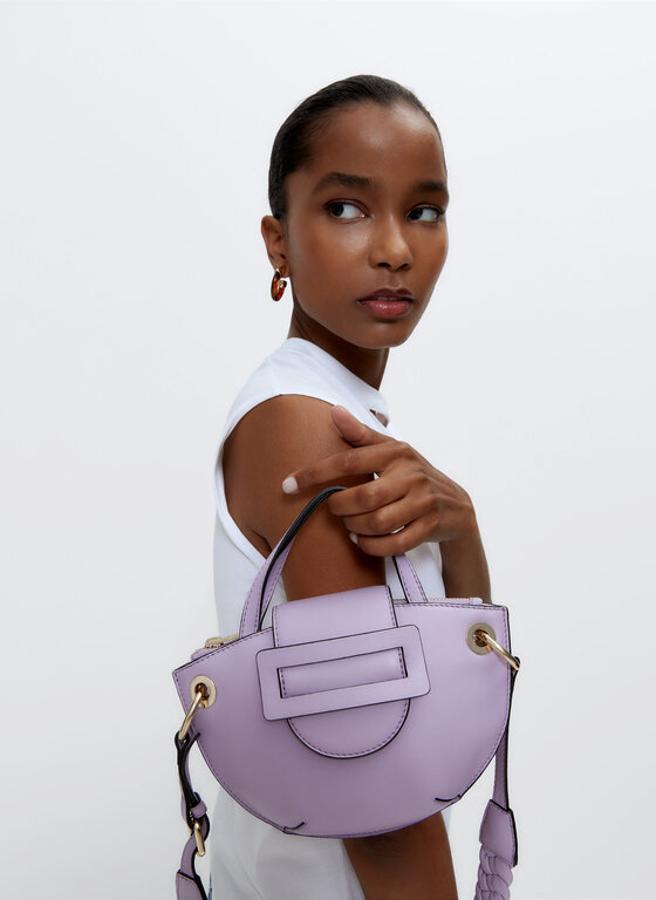 Con asa bandolera trenzada y dos asas de mano, este bolso confeccionado en piel de cordero de Uterqüe viene con solapa con cinturón y botón a presión oculto y cierre superior de cremallera. Tiene un precio de 99 euros.