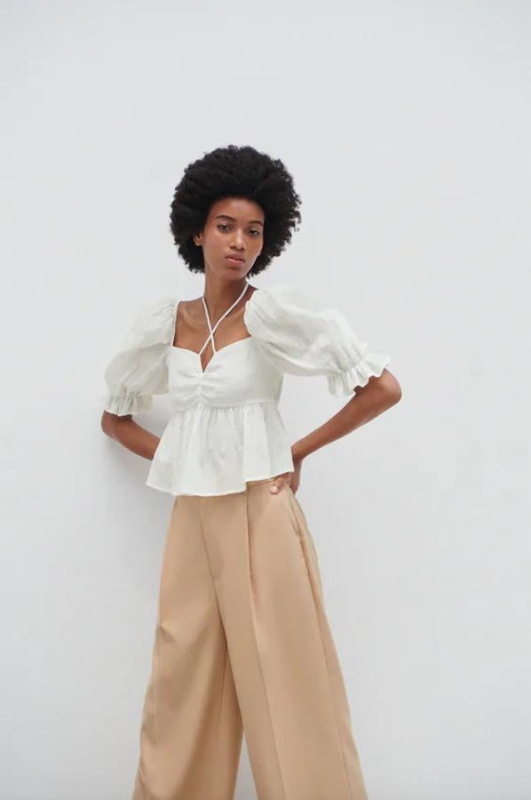 Con escote de pico con lazo y mangas cortas acabadas en elástico y volantes, al igual que la cintura y el bajo, este top confeccionado en péplum en Zara tiene un precio de 25,95 euros y está disponible entre las tallas XS y L.