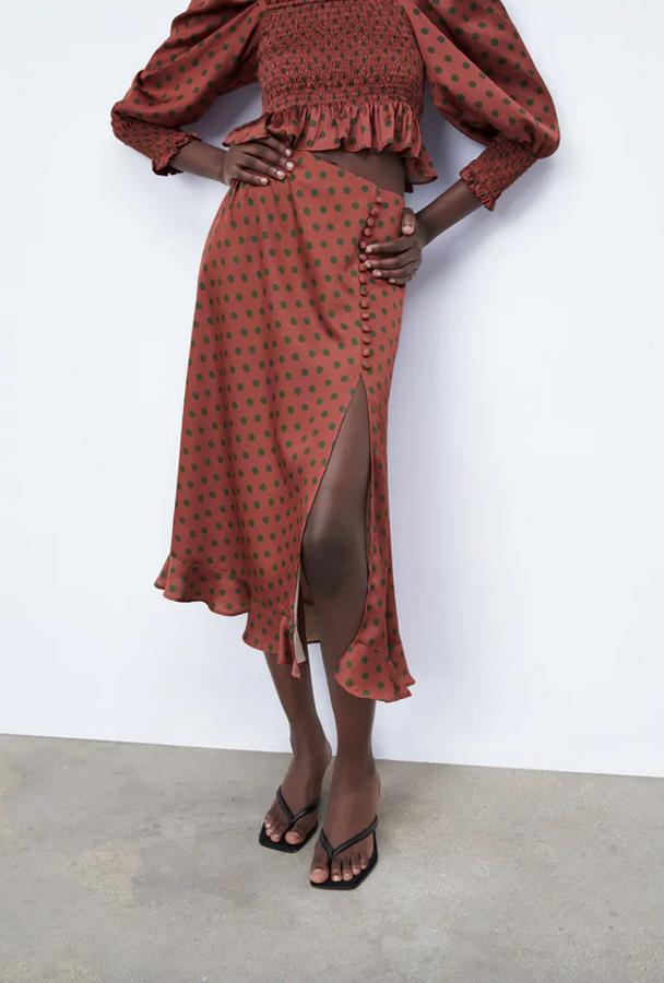 En color marrón con estampado de lunares en verde, esta falda fluida de Zara con abertura frontal, falsos botones delanteros forrados a tono y bajo acabado en volante, tiene un precio de 29,95 euros y está disponible entre las tallas XS y L.