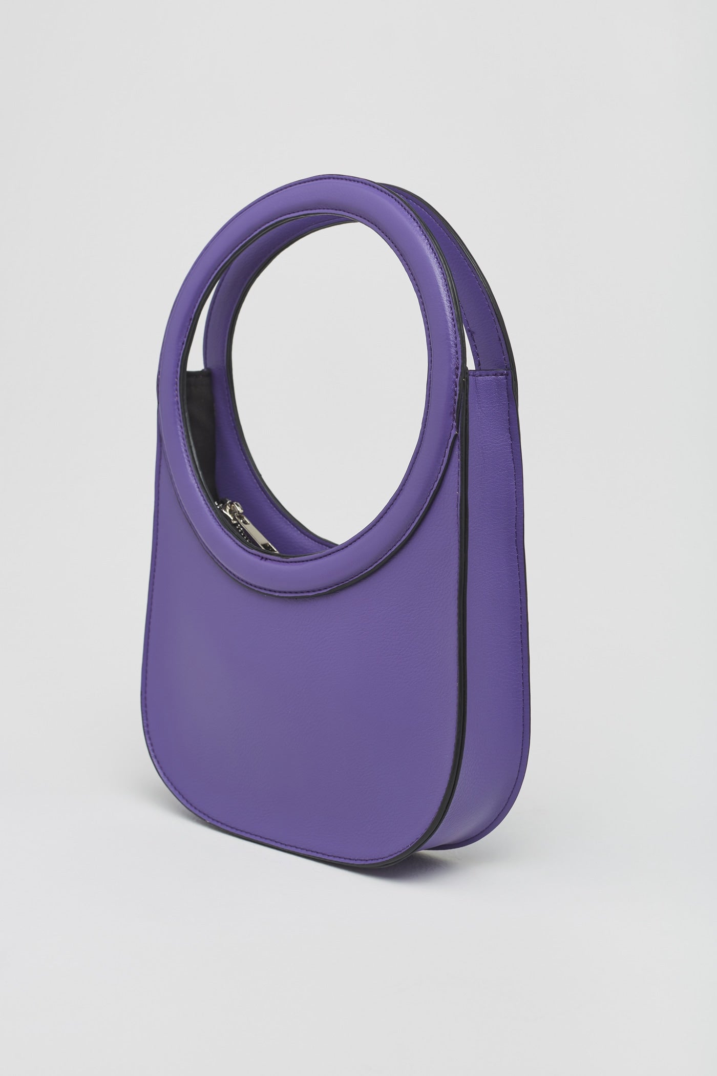 Una de las propuestas más vistosas y originales es este bolso de asa circular con cierre de cremallera en color morado que costaba 17,99 euros y ahora podemos comprar por 15,99 euros. 