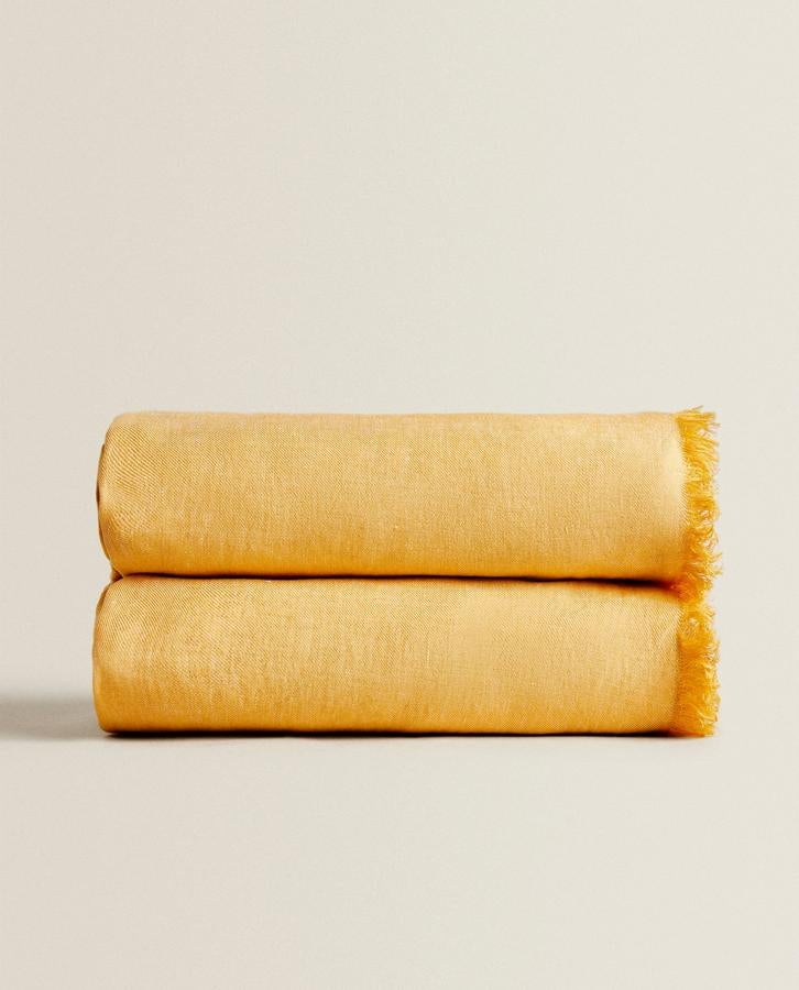 En color amarillo, lino y con acabado de flecos. Esta manta de Zara Home es todo lo que necesitas para dar vida a tu terraza. Cuesta 69,99 euros.