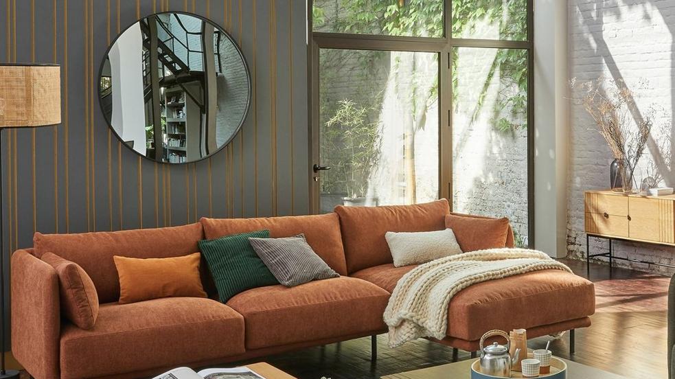 Salón con sofá chaise longue y espejo grande en la pared.