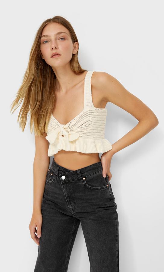 Este top de crochet en color vainilla y de tirantes cuenta con detalle de nudo en el escote y bajo con volante. Tiene un precio de 15,99 euros.