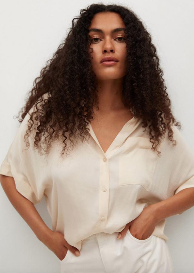 En blanco roto y tejido satinado, esta camisa de diseño oversize con cuello mao, escote de pico y mangas cortas, viene con bolsillo de plastrón en la pechera y costura del hombro caída. Cuesta 19,99 euros y está disponible entre las tallas XS y XL.