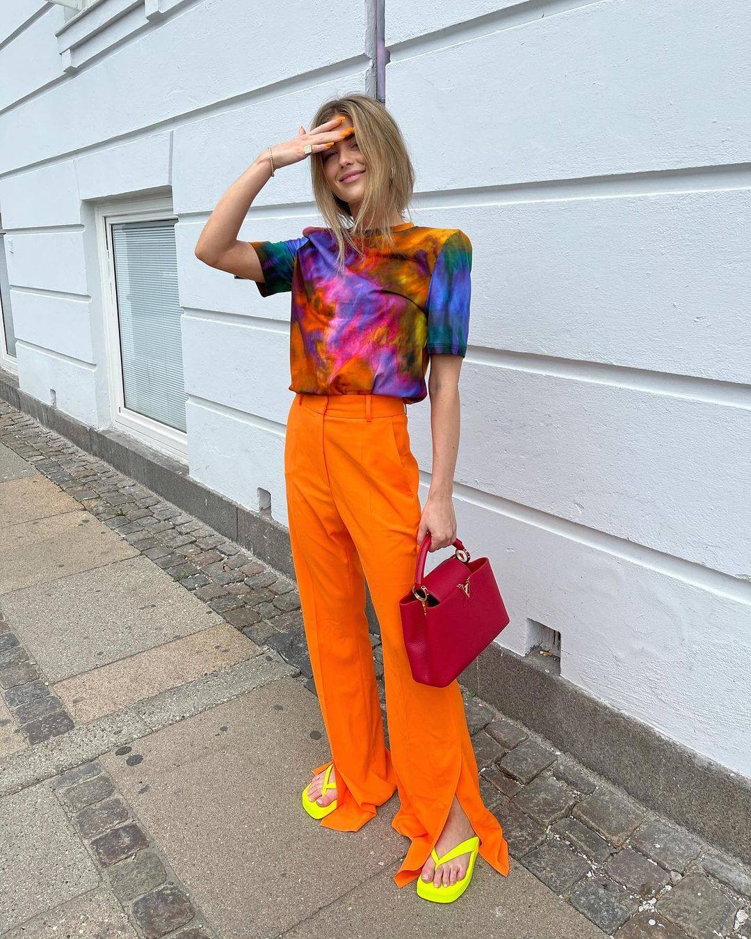 Colores vibrantes es sinónimo de Emili Sindlev. La 'it girl' conjunta una camiseta desteñida con el resto de prendas, en tonos que extrae de su top. Pantalones naranja, chanclas amarillas y bolso rojo.