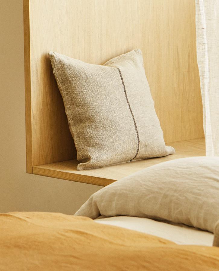 Con una medida de 45x45 centímetros, esta funda de cojín de lino con una raya fina estampada en el centro es de Zara Home y tiene un precio de 29,99 euros.
