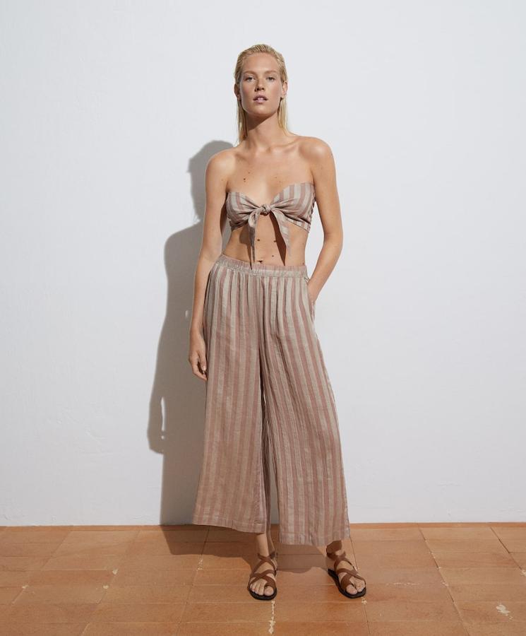 En marrón tostado con estampado de rayas verticales, este conjunto de Oysho formado por pantalón largo de diseño culotte y top de lazo está confeccionado en algodón y lino y sienta de maravilla con sandalias planas y con cuñas. El pantalón cuesta 35,99 euros y el top 15,99 euros. 