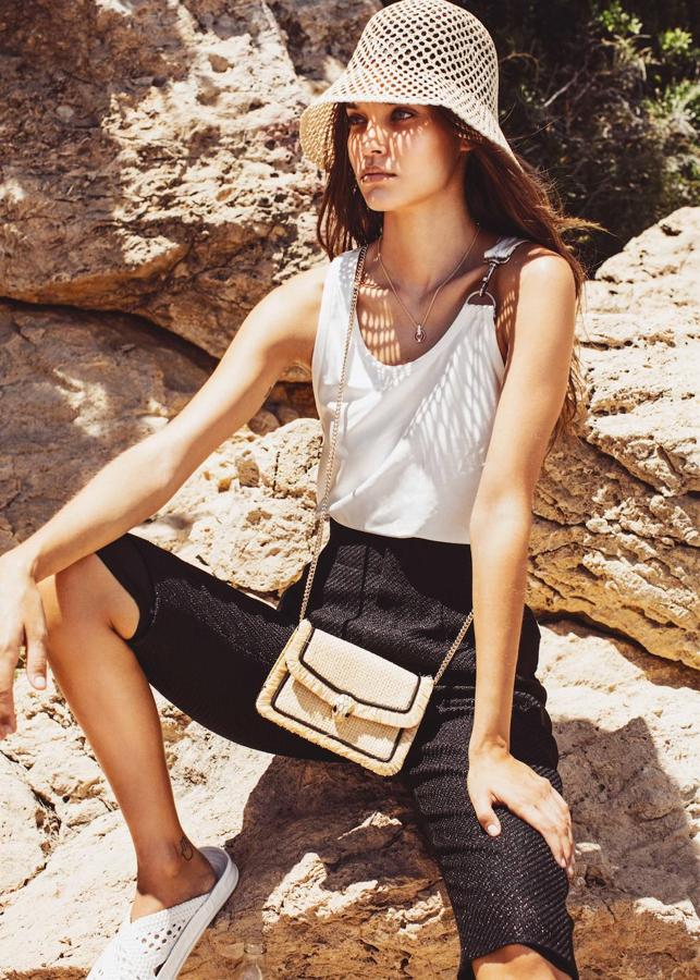 Gara lleva sombrero de &Other Stories, camiseta y bermudas de Louis Vuitton, colgante de oro, coral y brillante y mini bolso Serpenti en rafia, ambos de Bvlgari. Las sandalias son de Fendi.