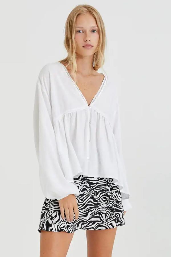 De manga larga y con escote de pico, esta camisa blanca con botone s delanteros y detalles de cintas y volantes tiene un precio de 22,99 euros.