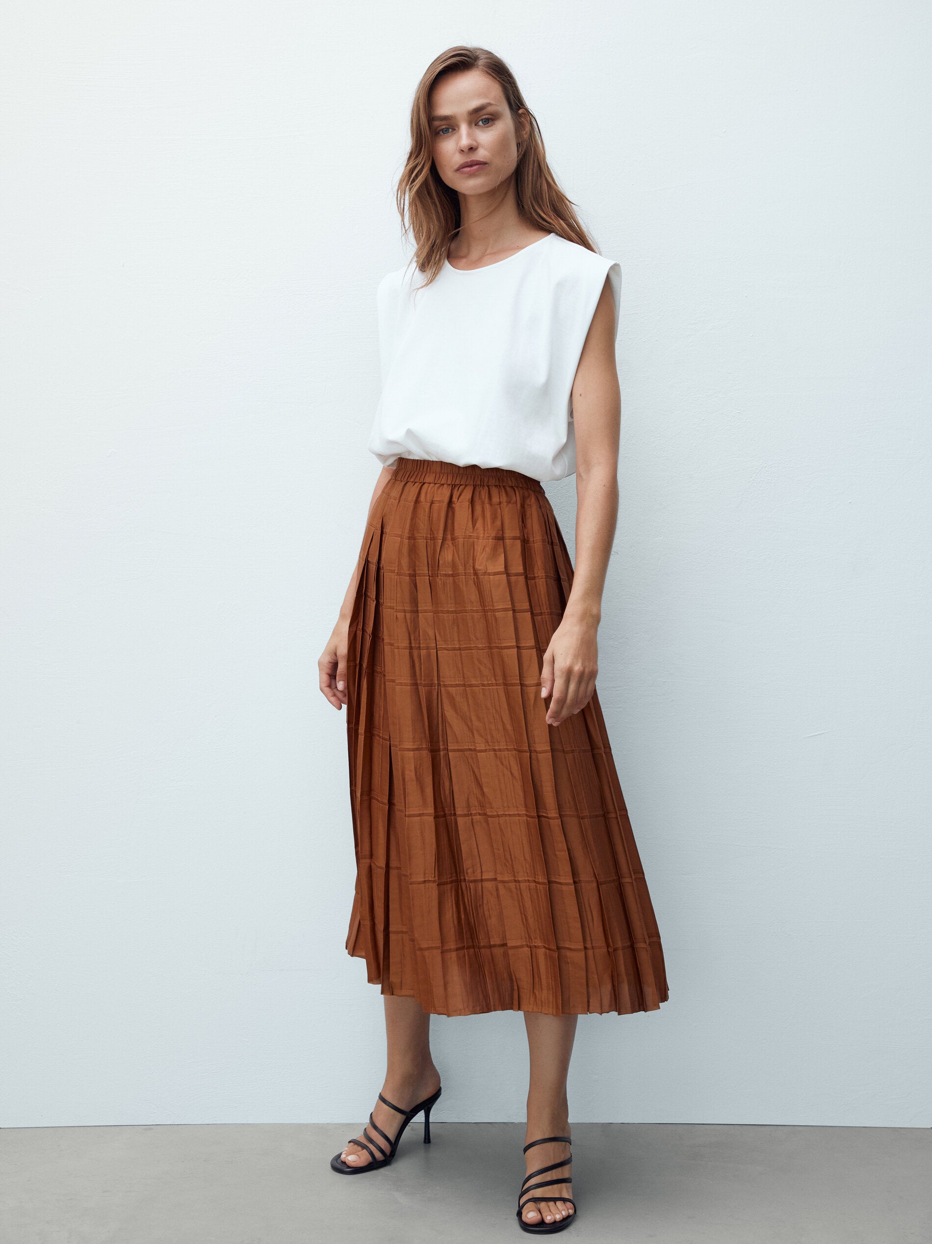 Nada mejor para una transición fácil y sin traumas que una falda midi plisada de corte evasé perfecta para combinar con una camiseta básica sin mangas y sandalias de tacón, perfecta para la vuelta al trabajo. 