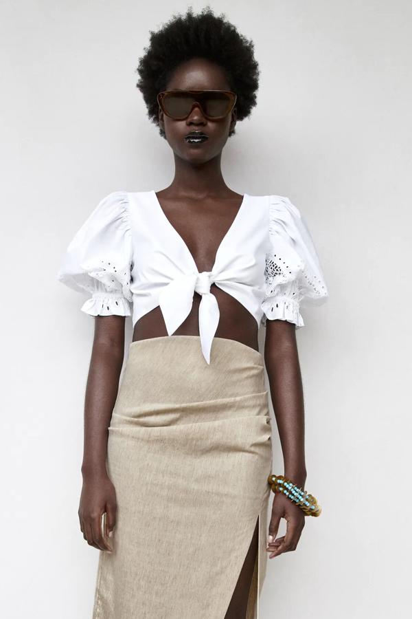 En color blanco, este top cropped con escote de pico y manga abullonada por debajo del codo cuenta con detalles perforados y cierre con nudo en la parte delantera. Tiene un precio de 22,95 euros.