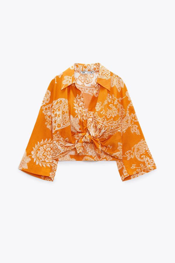 En color naranja, este top corto con cuello solapa y escote de pico cuenta con detalle de nudo en el bajo y cierre frontal con botón. Tiene un precio de 29,95 euros.