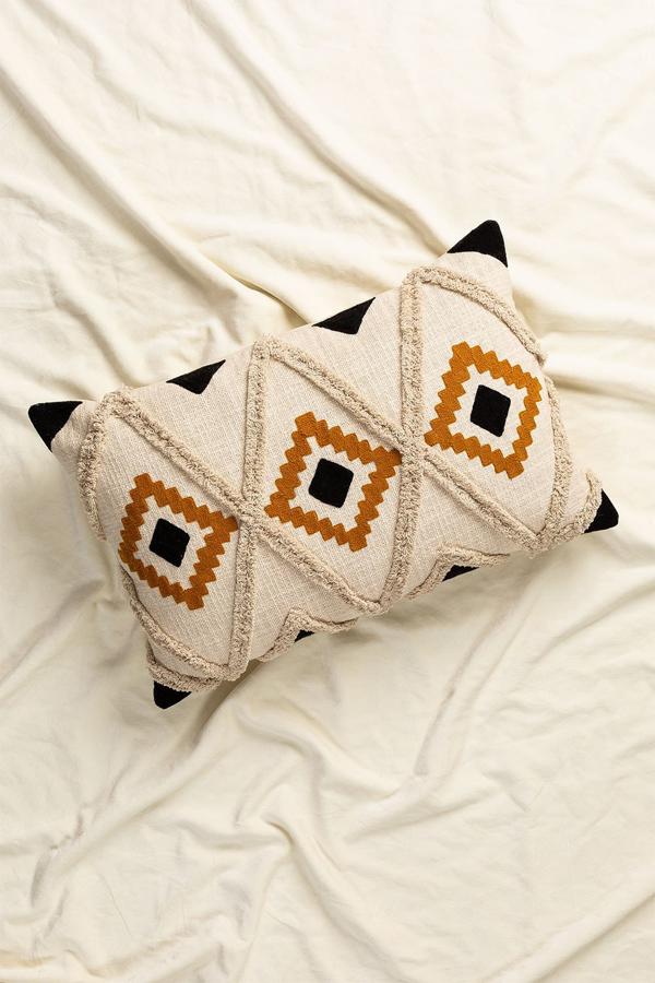 Cojín rectangular con estampado geométrico en tonos tierra, blanco y negro. Tiene unas dimensiones de 40x60 cm y cuesta 29,95 euros.