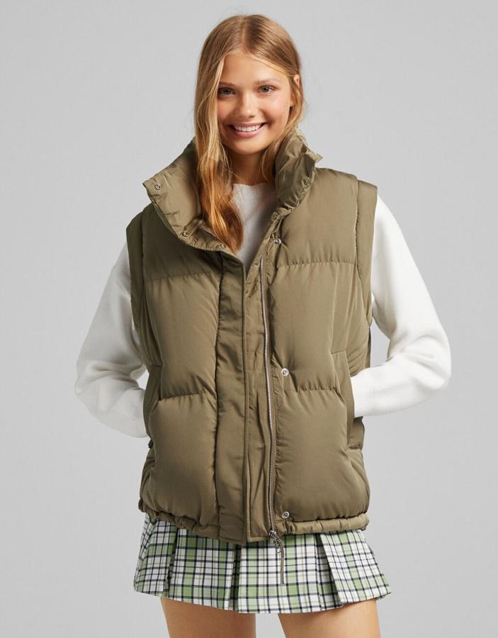 Disponible en negro, caqui y blanco, este chaleco acolchado en efecto nylon de Bershka es de diseño medio y viene con bolsillos al bies, cierre frontal de cremallera oculto por tapeta y cuello alto. Con bajo ajustable con goma, cuesta 29,99 euros.