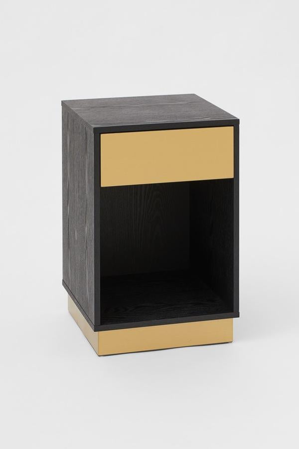 En color negro, esta mesita de noche en MDF y metal cuenta con cajón con frente en color dorado y tiene unas medidas de 59x38x38 centímetros y un precio de 149 euros.