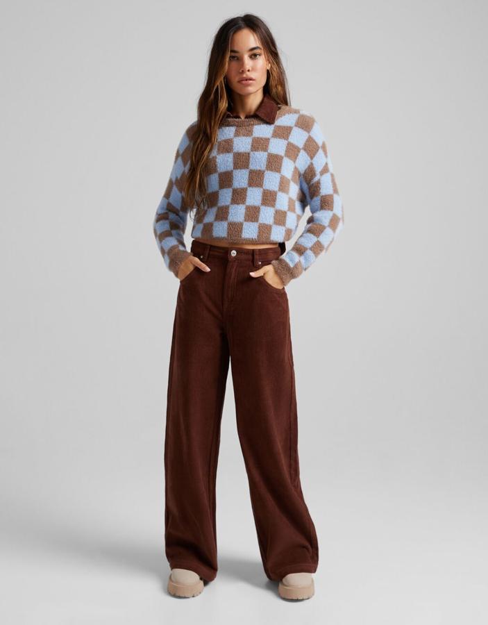 En azul celeste y marrón con estampado damero, este jersey cropped de Bershka con cuello redondo y mangas largas tiene un precio de 22,99 euros y está disponible entre las tallas XS y XL.