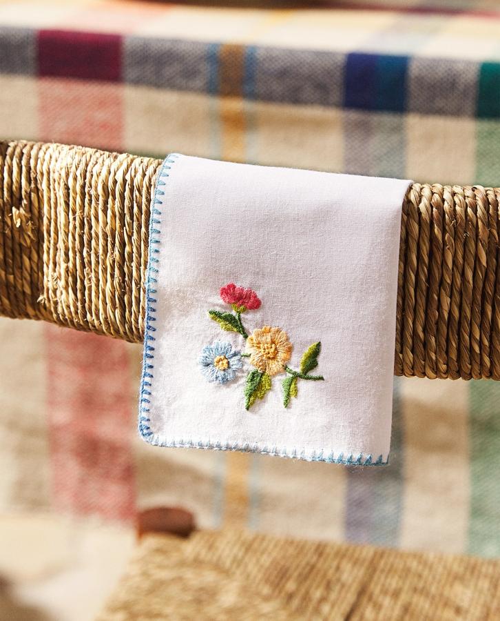 Juego de cuatro servilletas bordadas (20x20 cm) con detalle floral y pespunte en azul en los extremos. Tiene un precio de 25,99 euros.