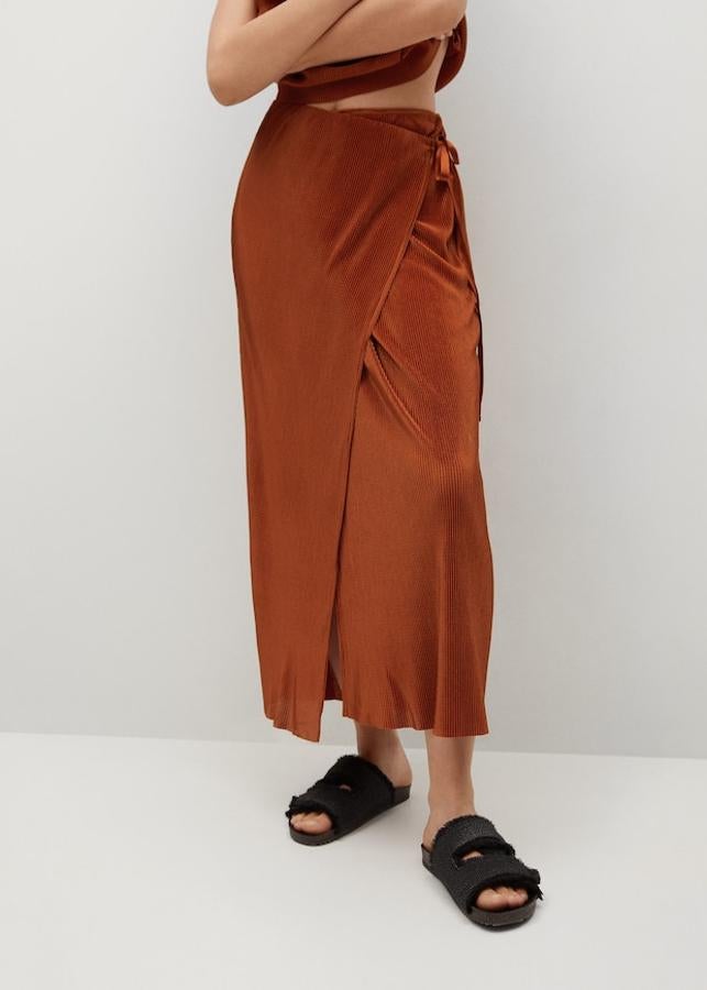 En Mango han apostado por el naranja tostado para esta preciosa falda plisada confeccionada en tejido satinado y de diseño midi cruzado y recto. De tiro alto y con cierre de lazo lateral, cuesta 29,99 euros y solo queda en las tallas S y XL.