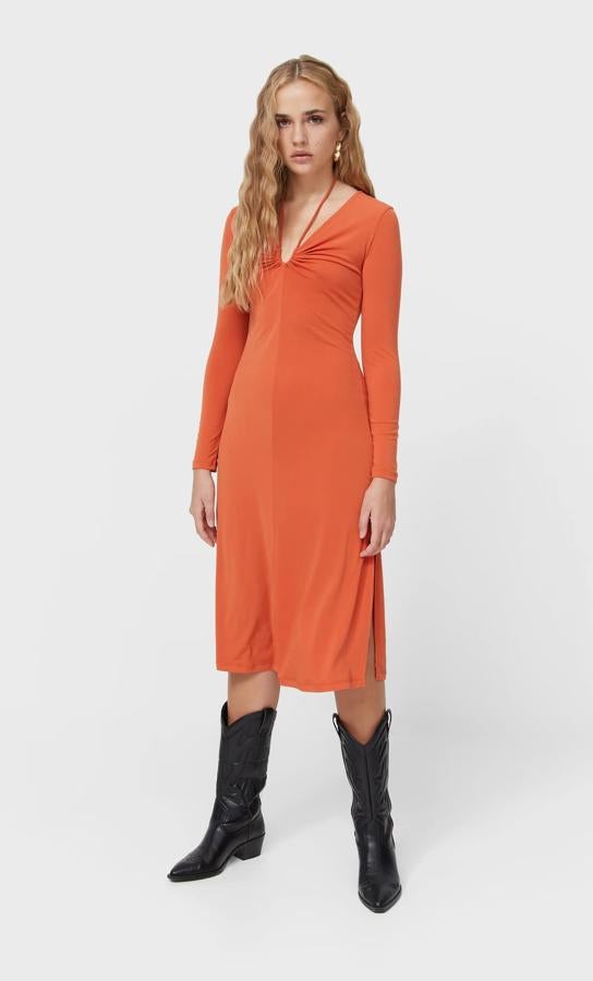 Diseño midi para este vestido naranja de Stradivarius con escote de pico con tiras, mangas largas y bajo con abertura lateral. Disponible entre las tallas XS y XL, cuesta 19,99 euros.