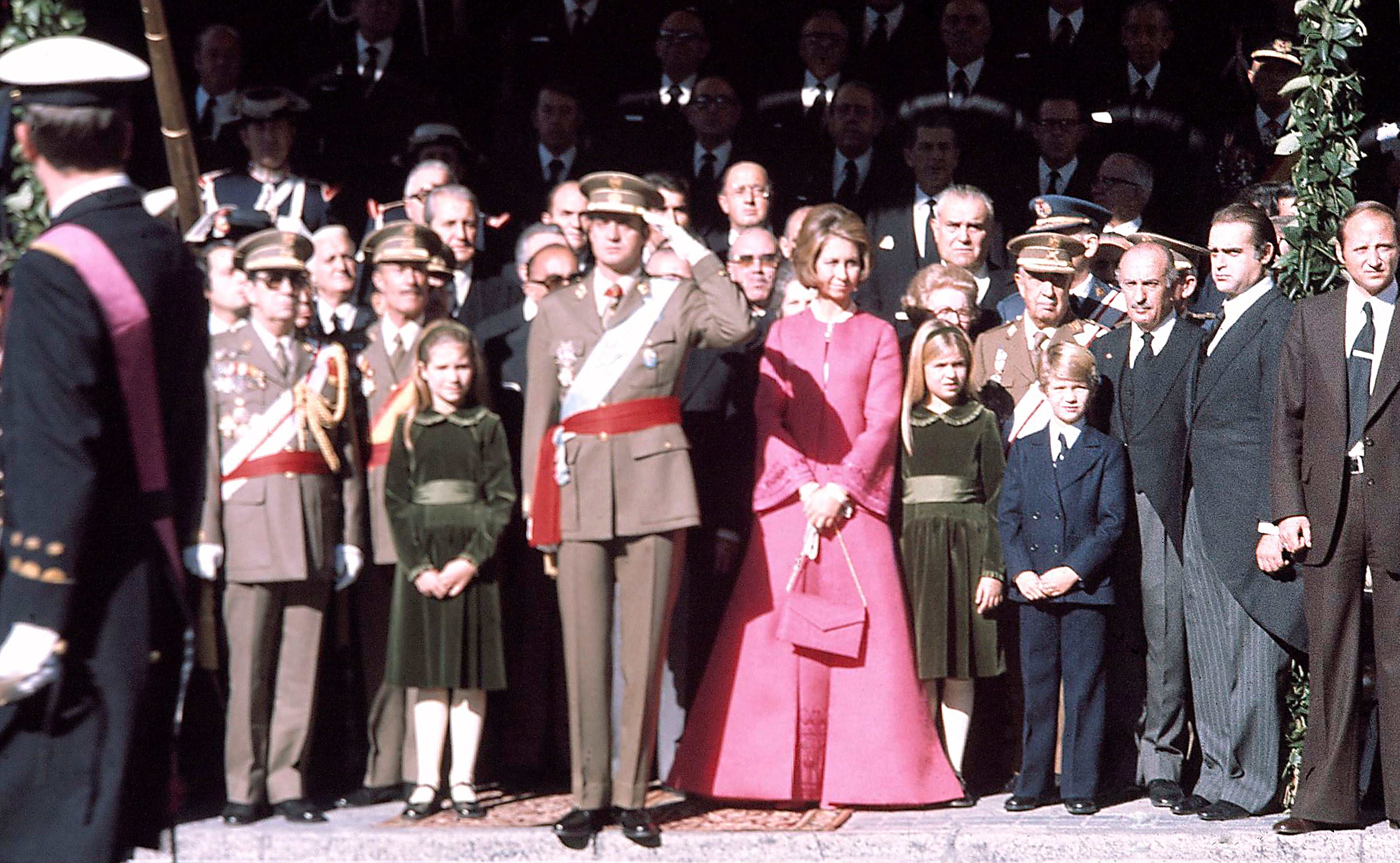 El 22 de noviembre de 1975 don Juan Carlos se convertía, ante las Cortes, en Rey de España. Atrás quedaban 40 años de dictadura y se empezaba a fraguar la Transición democrática de España. Para aquel día histórico, y frente al luto de los Franco, la ya Reina Sofía se atrevió con un imponente conjunto de abrigo y vestido de silueta trapecio en un llamativo rosa fucsia.