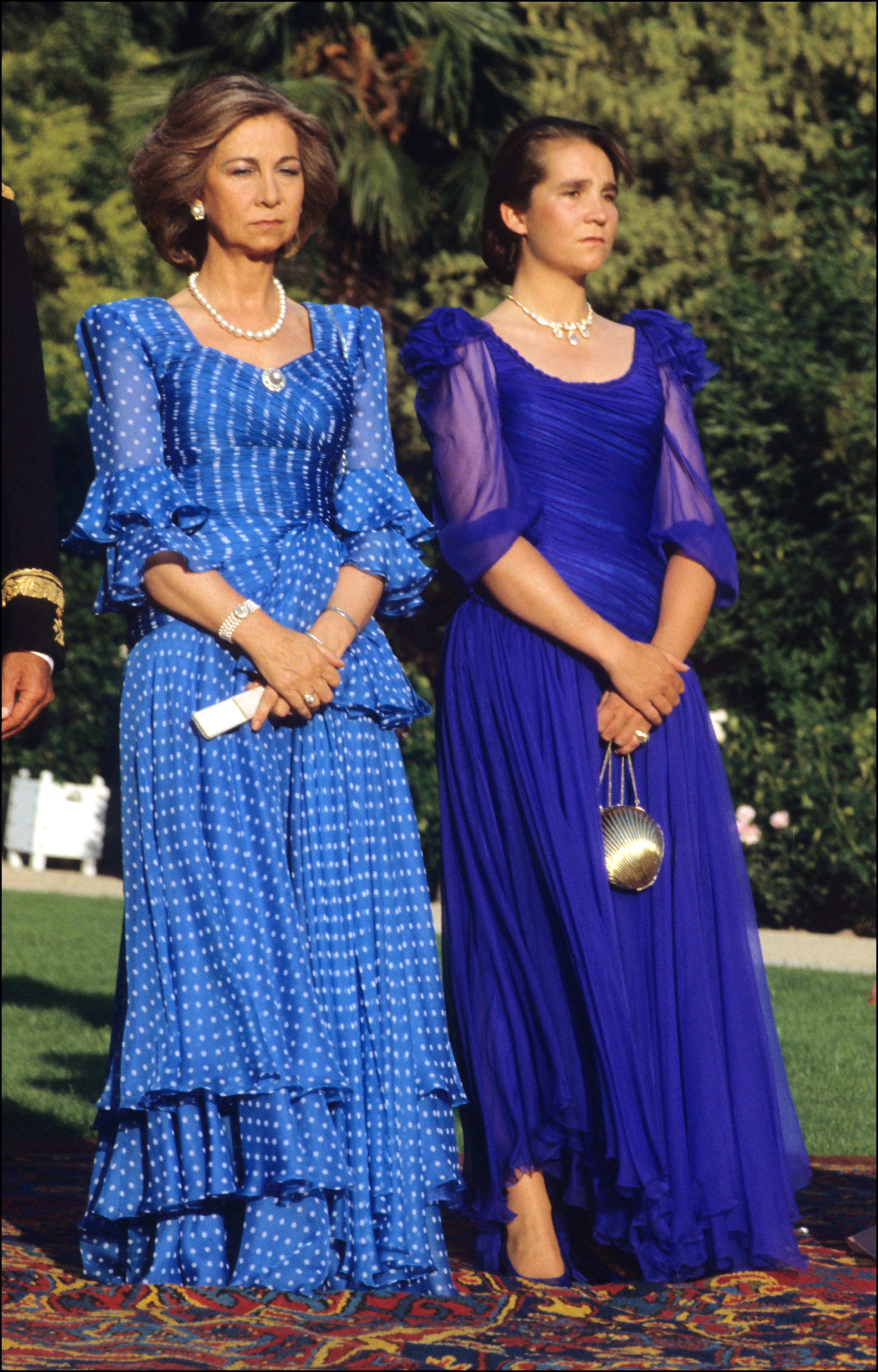 Esta imagen de la Reina Sofía y la Infanta Elena en los Jardines de Sabatini de Madrid data de la década de los 80, pero el vestido de la Reina, un imponente diseño de gasa azul klein con estampado de lunares, flada con volantes, escote cruzado drapeado y lazo a la cintura no puede ser más tendencia y más actual. Lo firmaba Valentino, y ojalá pronto lo recupere la Reina Letizia.