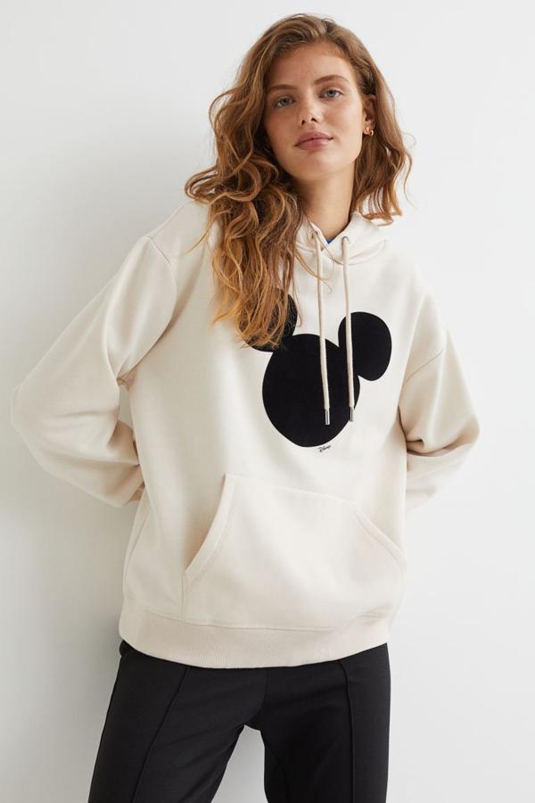 En beige claro con motivo frontal de Mickey Mouse, esta sudadera con capucha de H&M de venta exclusiva en su tienda online viene con bolsillo canguro en el frontal y puños y bajo en punto elástico de canalé. Cuesta 29,99 euros y está disponible entre las tallas XS y XXL. 