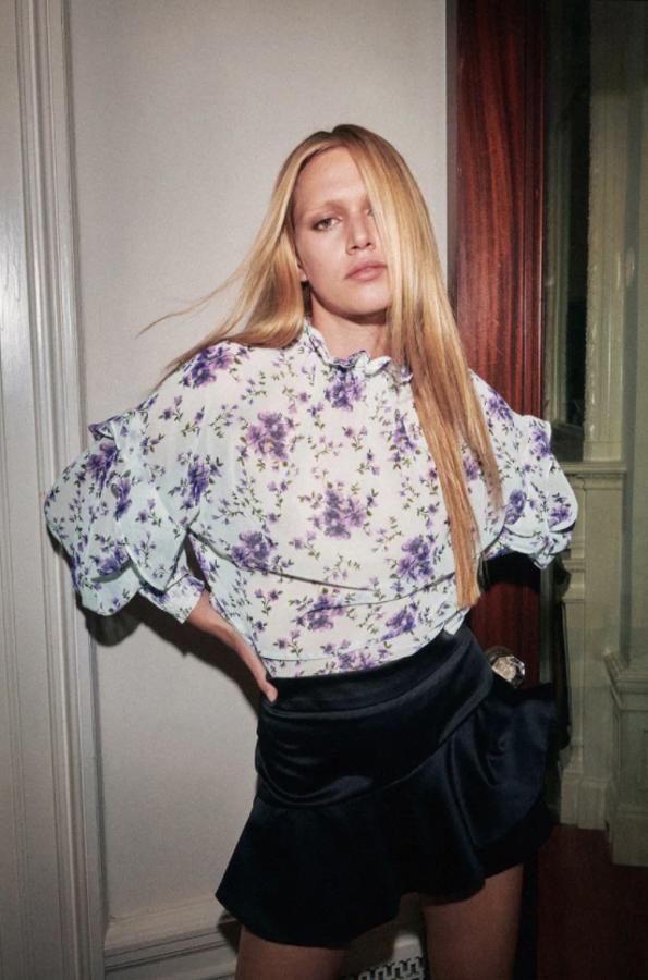 En tejido semitransparente, con cuello con volante y mangas largas acabadas en puño elástico, esta camisa blanca con estampado floral en lila y verde cuesta 25,95 euros. 