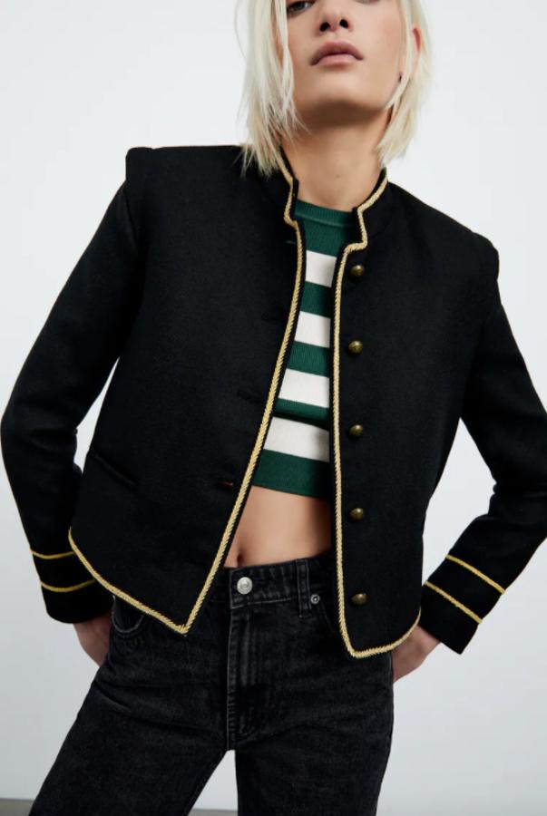 Diseño corto en color negro para esta cazadora de Zara de cuello subido y mangas largas con hombreras que viene con falsos bolsillos de vivo en delantero y detalle de vivos combinados en hilo dorado. Con cierre frontal de botones, cuesta 49,95 euros y está disponible entre las tallas XS y XXL. 