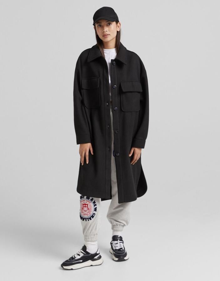 En color negro, con cuello camisero y cierre de botones frontal a tono, esta sobrecamisa larga de Bershka en efecto lana tiene bolsillos de plastrón en la pechera y bajos asimétricos ligeramente redondeados. Cuesta 39,99 euros. 