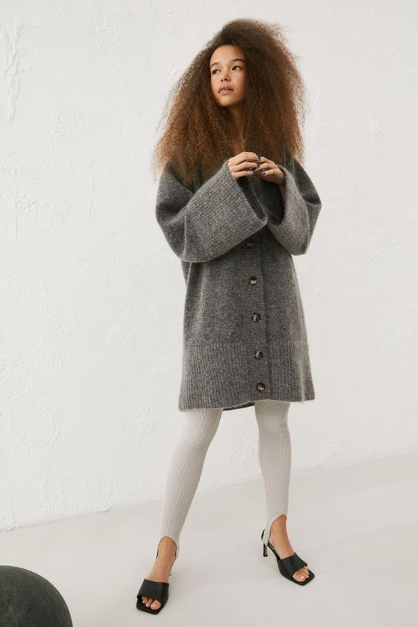 Diseño largo en punto de mezcla suave de lana para este cárdigan de diseño relajado que viene con hombros caídos, escote de pico, cierre de botones a contraste y mangas amplias ligeramente acampanadas. Con ribete ancho de canalé en escote, tapeta y puños, es de diseño largo hasta la rodilla y cuesta 79,99 euros. Está disponible en gris, en crema y en negro y solo se vende en la tienda online de H&M. 