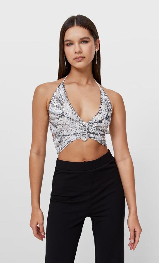 Con forma de mariposa, escote de pico y tirante fino cruzado en la espalda, este top de Stradivarius con lentejuelas plateadas cuesta 22,99 euros. 