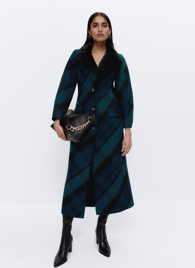 Interior en efecto pelo en color negro para este abrigo de cuadros en tonos verdes y azules que podemos encontrar en Uterqüe y viene con cierre frontal de botón fantasía en el frontal, mangas con volumen y abertura en la espalda. Cuesta 259 euros. 