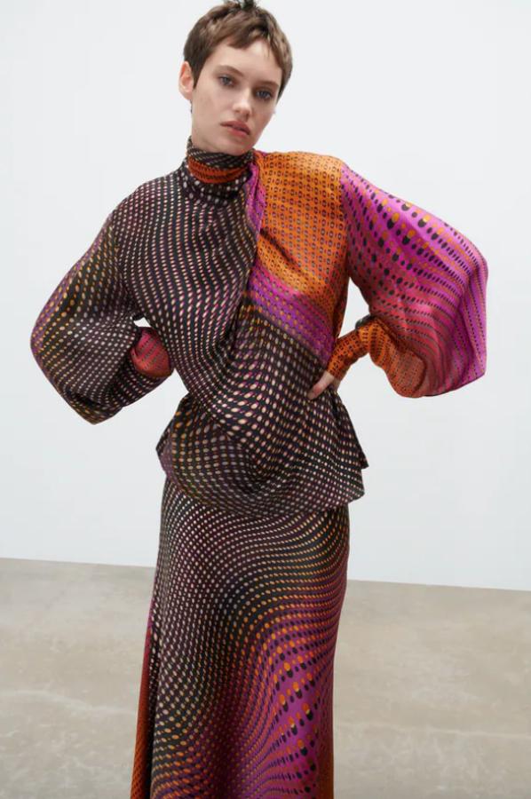 Cuello subido fluido y mangas largas con abertura en costura acabada en puño para esta blusa con estampado multicolor en tonos marrones, fucsia y naranjas que viene con detalle de lazada en el mismo tejido con pliegues. Podemos comprarla por 39,95 euros. 