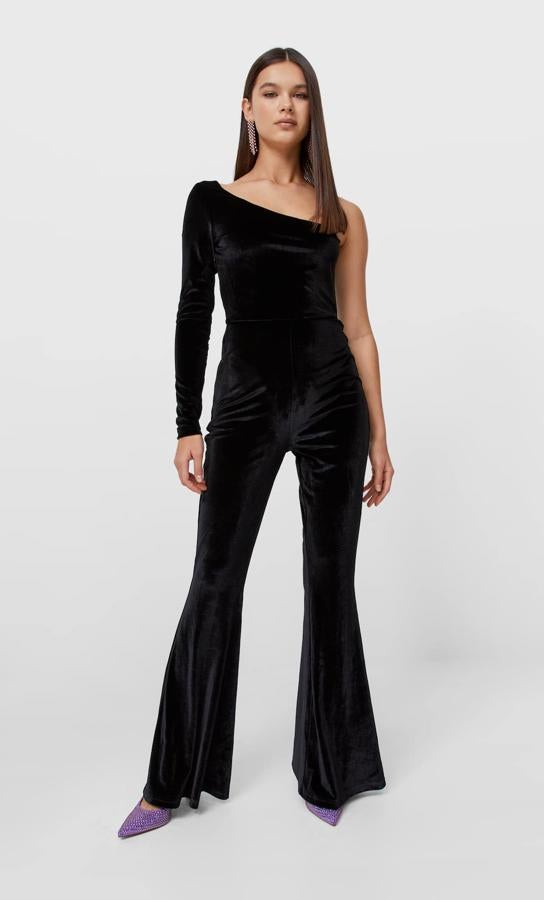Este mono de terciopelo en negro, con escote asimétrico y mangas largas es de Stradivarius y viene con las perneras de acabado acampanado. Cuesta 35,99 euros. 