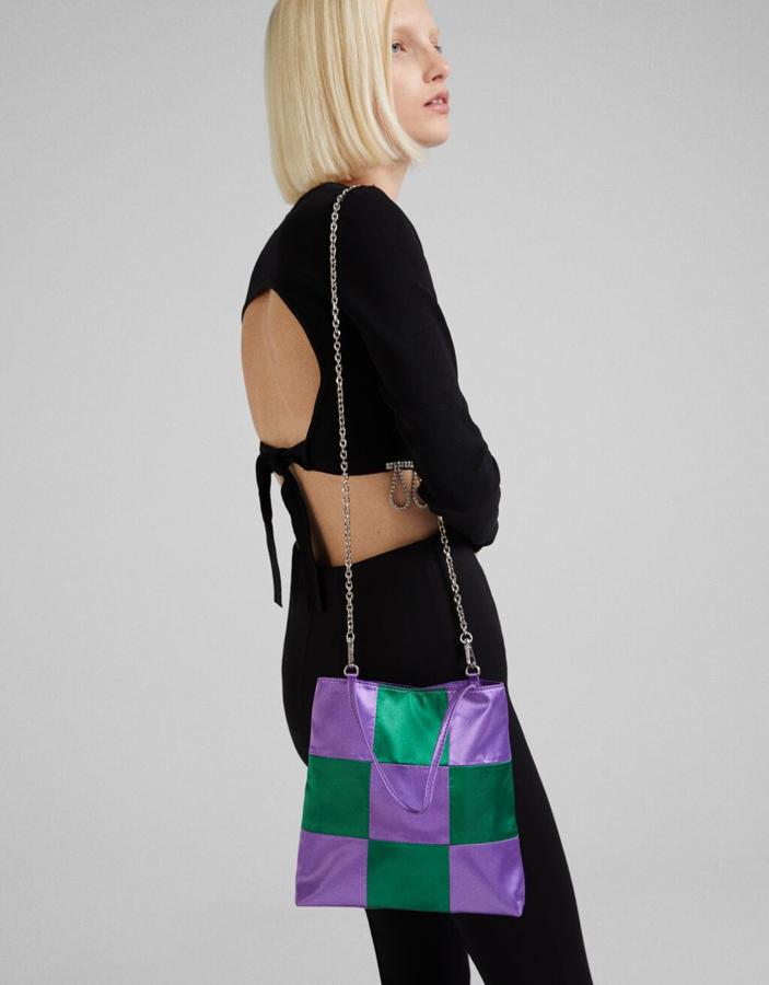 Estampado damero en lila y verde para este bolso de Bershka con asas de mano en lila y de hombro en cadena plateada. De tamaño medio y con cierre superior de cremallera, tiene un precio de 17,99 euros.