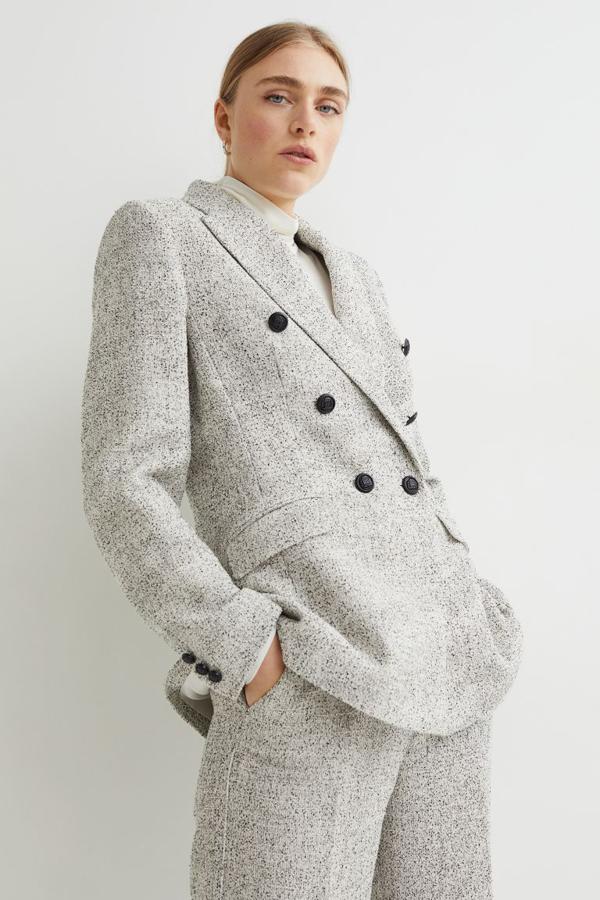 Esta bonita blazer confeccionada en hilo bouclé texturizado con lana en la trama que combina el blanco y el negro es de H&M y viene con doble botonadura, bolsillos decorativos con solapa en el frontal y abertura en el bajo en la espalda. Cuesta 59,99 euros. 