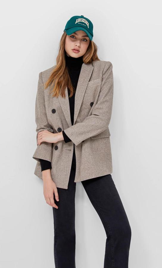 Diseño cruzado con botones a contraste para esta americana de Stradivarius en color piedra y estampado de espiga que viene con diseño de hombros marcados y puños abotonados. Podemos comprarla por 35,99 euros. 