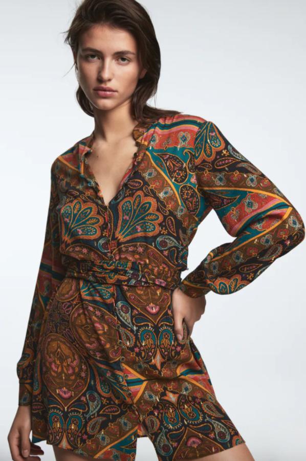 En tonos marrones y verdosos, este vestido camisero corto de Zara con estampado étnico viene con cuello redondo subido, mangas largas acabadas en puño y cinturón de lazada en el mismo tejido. Con detalle de aplicación de hilo metalizado y cierre frontal de botones, cuesta 39,95 euros. 