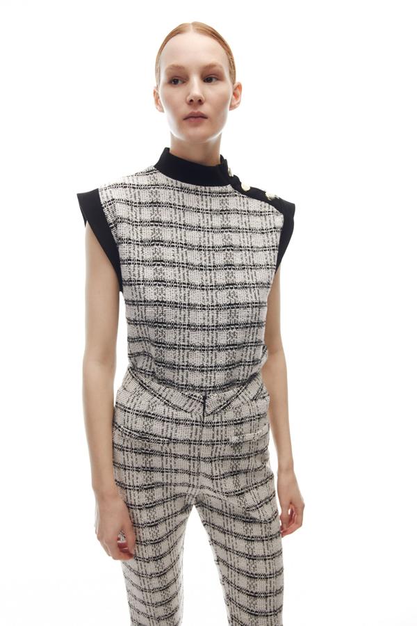 Estampado de cuadros en negro y gris piedra con cuello alto y mangas sisa a contraste para este top con aplique de botones en un hombro que podemos comprar por 25,99 euros. 