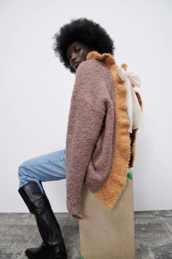 En marrón y volantes en beige, con cuello subido y mangas largas, este jersey de punto de diseño oversize viene con espalda abierta con detalle de lazo en organza. Cuesta 49,95 euros. 