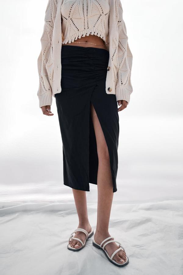 En color negro y de tiro alto, esta falda midi con frunces y bajo con abertura frontal que podemos comprar en Zara por 25,95 euros, está disponible entre las tallas XS y XL. 