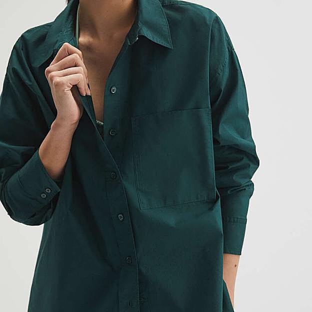 Imagen principal - Esta camisa 100% algodón de Oysho llega en colores básicos, como el azul celeste, pero también otros tonos más inesperados, como el verde botella o el arena. Camisa oversize de manga larga Oysho (39,99 euros) 