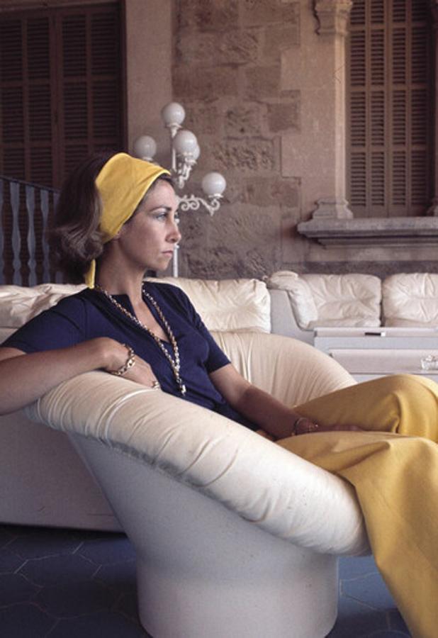 En 1975, verano en Marivent, poco después de ascender al trono. La reina muestra uno de sus “must”, la banda ancha para sujetar el pelo, algo que le resultaba muy útil, además, durante las regatas. Es también la época de las combinaciones bicolor y, como es habitual en ella, de las grandes joyas doradas. 