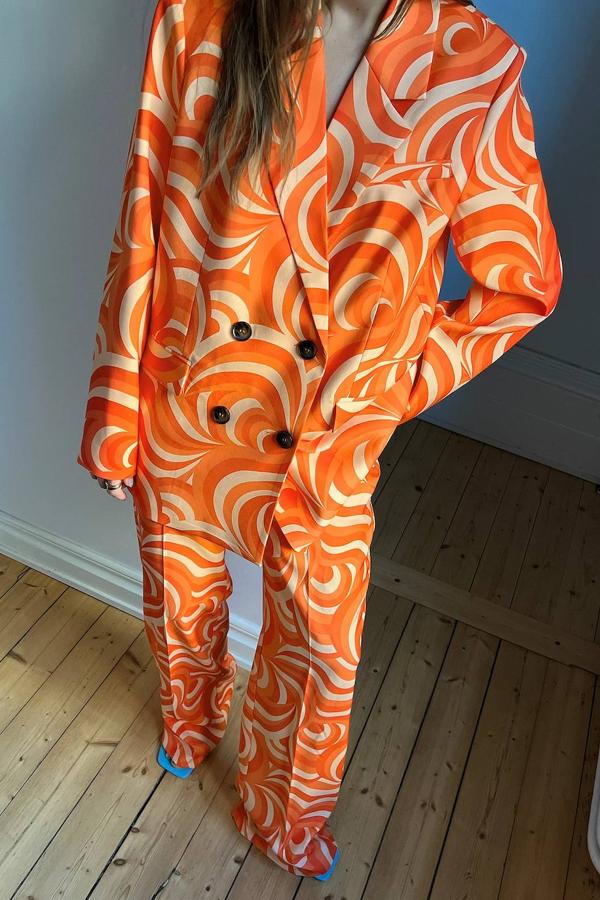 Traje de NA-KD adornado con estampado retro en tonalidades naranja. Se compone de americana oversize con cierre cruzado y doble botonadura que cuesta 101,95 y pantalón holgado con raya marcada, a 69,95 euros.