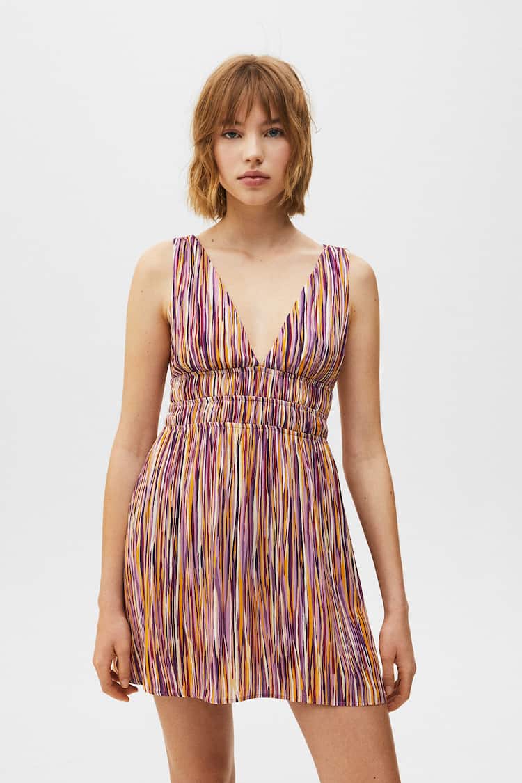 Escote de pico, manga sisa y detalle de elásticos en la espalda y la cintura, este vestido corto de Pull&Bear en tonos morados y anaranjados, solo se puede comprar en la web de la firma por 22,99 euros.
