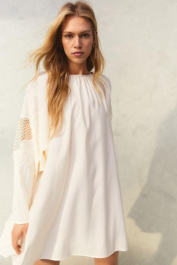 En color crema y con diseño maxivolumen, este vestido con espalda escotada y tiras finas de anudar en la nuca es de H&M y viene con mangas largas con detalles de malla ancha y bordados y sisas amplias fruncidas. Tiene un precio de 19,99 euros. 