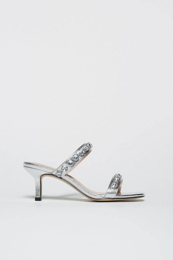 Sandalia de tacón bajo con acabado metalizado en tono plateado y tiras adornadas con aplicaciones de strass, de Sfera. La encontrarás con un precio de 29,99 euros.