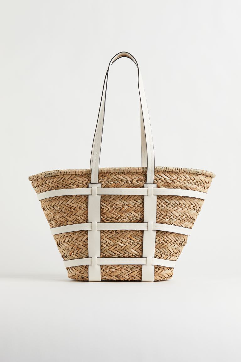 Un capazo con aires urbanos, gracias a los detalles de piel de color blanco. Un sustituo perfecto para el clásico shopping bag en versión 100% veraniega. Bolso de rafia con detalles de piel de H&M (39,99 euros)