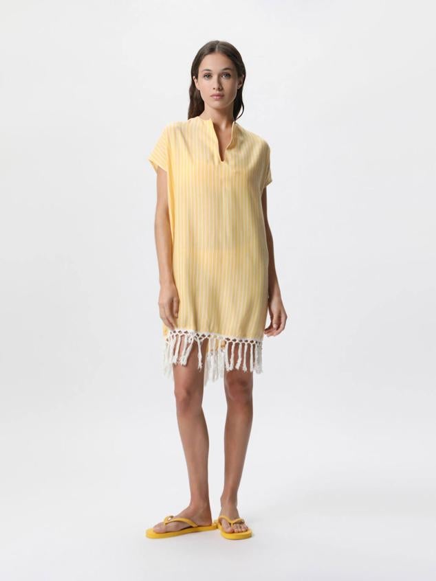 Vestido caftán corto con escote en v, silueta recta y holgada, manga corta, bajo acabado en flecos, con estampado a rayas en amarillo claro y blanco, de Lefties. ¿Su precio? 15,99 euros.