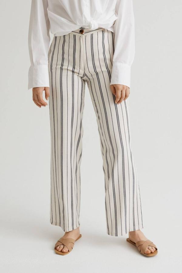 Pantalón largo en tejido mezcla de lino con pernera recta, talle alto con cintura elástica, bolsillos y cierre de botón y cremallera, en print a rayas blanco y azul, de H&M. Está disponible por 24,99 euros.